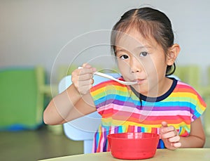 Cute little Asian girl eating cereal with cornflakes and milk on the table. Children having breakfast at morning