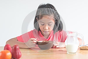 Cute little Asian girl eating cereal with the milk in the kitche