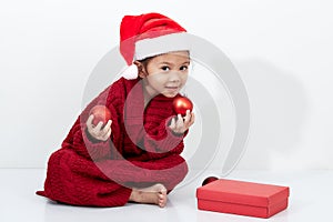 Girl holding a red christmas ball in sweater and santa hat