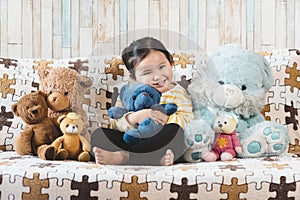 Cute little asian girl hugging her plush toy teddy bear on a sofa.