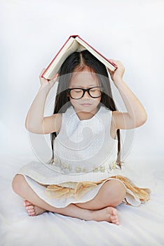 Cute little Asian girl lying on bed and place hardcover book on her head and closed eyes over white background