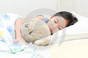 Cute little asian girl sleep and hug teddy bear on bed.