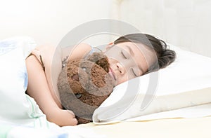 Cute little asian girl sleep and hug teddy bear on bed