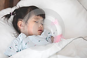 Cute little asian girl sleeping with doll in bed