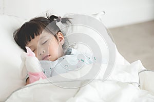 Cute little asian girl sleeping with doll in bed