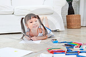 Cute little asian girl smiling happy Lay down drawing on the floor in the living room of the house.