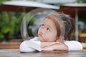 Cute little Asian kid girl with funny face lying on the wooden table with looking up