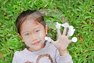 Cute little Asian kid girl lying on green grass lawn with showing empty white stickers on her fingers. Focus on hand