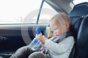 Cute little Asian 18 months / 1 year old toddler baby boy child sitting in car seat holding and drinking water from cup