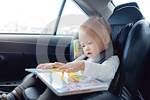 Cute little Asian 18 months / 1 year old toddler baby boy child sitting in car seat holding and enjoy reading book
