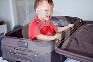 Cute little Asian toddler baby boy child sitting in travel suitcase getting ready for vacation, Kid playing in traveling baggage