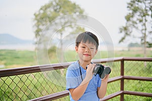Cute little Asian school boy child looking through binoculars explores nature field at viewpoint outdoors