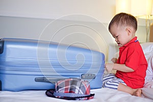 Cute little Asian toddler baby boy child pack a travel suitcase getting ready for vacation, Kid playing with traveling baggage