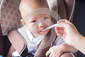 Cute little asian toddler baby boy eating from spoon in car seat in car