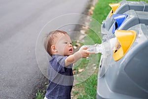 Cute little Asian toddler boy child throwing plastic bottle in recycling trash bin at public park