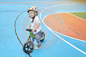 Cute little Asian toddler boy child wearing safety helmet learning to ride his first balance bike, kid playing & cycling at the