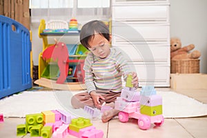 Cute little Asian toddler girl child having fun playing with colorful plastic toy blocks on floor at home, Educational toys for