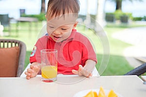 Asian  toddler baby boy child sitting in high chair holding & drinking tasty orange juice / cold drink in a