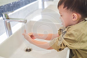 Sian 3 - 4 years old toddler baby boy child washing hands by himself on sink and water drop from faucet in public toilet