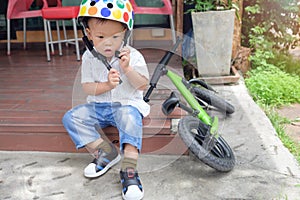 Asian 2 years old toddler boy child getting ready for cycle by wearing, fitting bicycle helmet before riding balance bike