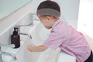 Asian 2 - 3 years old toddler boy child washing hands by himself on sink and water drop from faucet in public toilet / bathroom