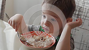 Cute little baby alone eats porridge with a spoon from a plate, the concept of healthy eating.