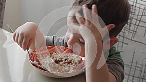 Cute little baby alone eats porridge with a spoon from a plate, the concept of healthy eating.