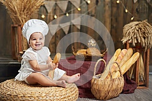 Cute little baby baker with a French baguette in a rustic wooden interior