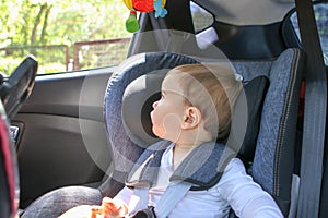 Cute little baby boy in car safety seat looking at the window.