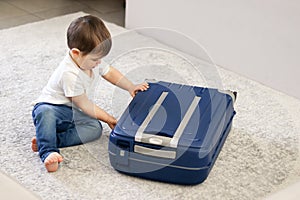 Cute little baby boy closing blue suitcase finished packing for vacation.