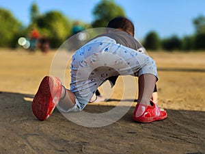 Cute little baby boy crawling in a park. Child crawling in a public park and looking forward. View from back. Copy space