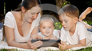 Cute little baby boy with family lying on grass in park with tablet computer. Parenting, family, children development