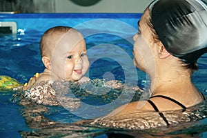 Cute little baby boy with funny grimace in a swimming pool holding by mother.