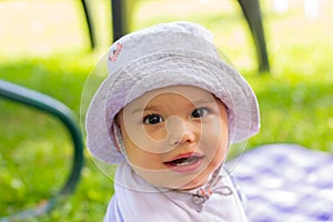 Cute little baby boy in funny hat sitting on the blanket on green grass. Picnic with child