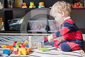 Cute little baby boy having fun at home playing with colorful wooden blocks, on the floor