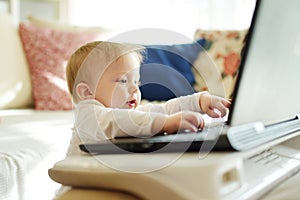 Cute little baby boy holding hands on laptop keyboard and looking at monitor