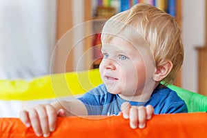 Cute little baby boy playing in colorful playpen, indoors