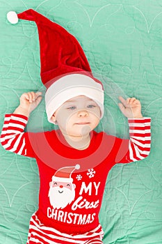 Cute little baby boy with Santa hat on his first Christmas. Adorable toddler child lying on green coverlet. Christmas