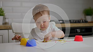 Cute little baby boy sitting behind table and drawing with fingers covered in colorufl paint. Concept of child education