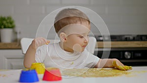 Cute little baby boy sitting behind table and drawing with fingers covered in colorufl paint. Concept of child education