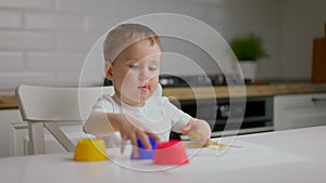 Cute little baby boy sitting behind table and drawing with fingers covered in colorufl paint. Concept of child education