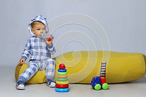 Cute Little Baby Boy Sitting On a Yellow Bean Bag Chair and Playing Toys.