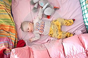 A cute little baby boy is sleeping peacefully and relaxed on his bed with toys