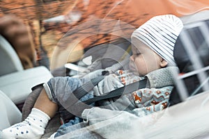 Cute little baby boy sleeping strapped into infant car seat in passenger compartment during car drive.