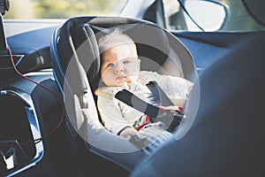 Cute little baby boy strapped into infant car seat in passenger compartment during car drive.