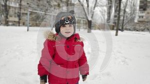 Cute little baby child boy in red sport jaket having fun playing on playground, city park outdoors during snowfall in winter.