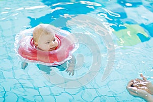 Cute little baby child learning to swim with swimming ring in an indoor pool