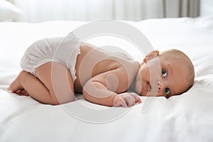 Cute little baby in diaper on bed at home