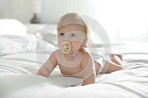 Cute little baby in diaper with pacifier lying on bed at home