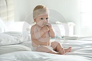 Cute little baby in diaper with pacifier sitting on bed at home